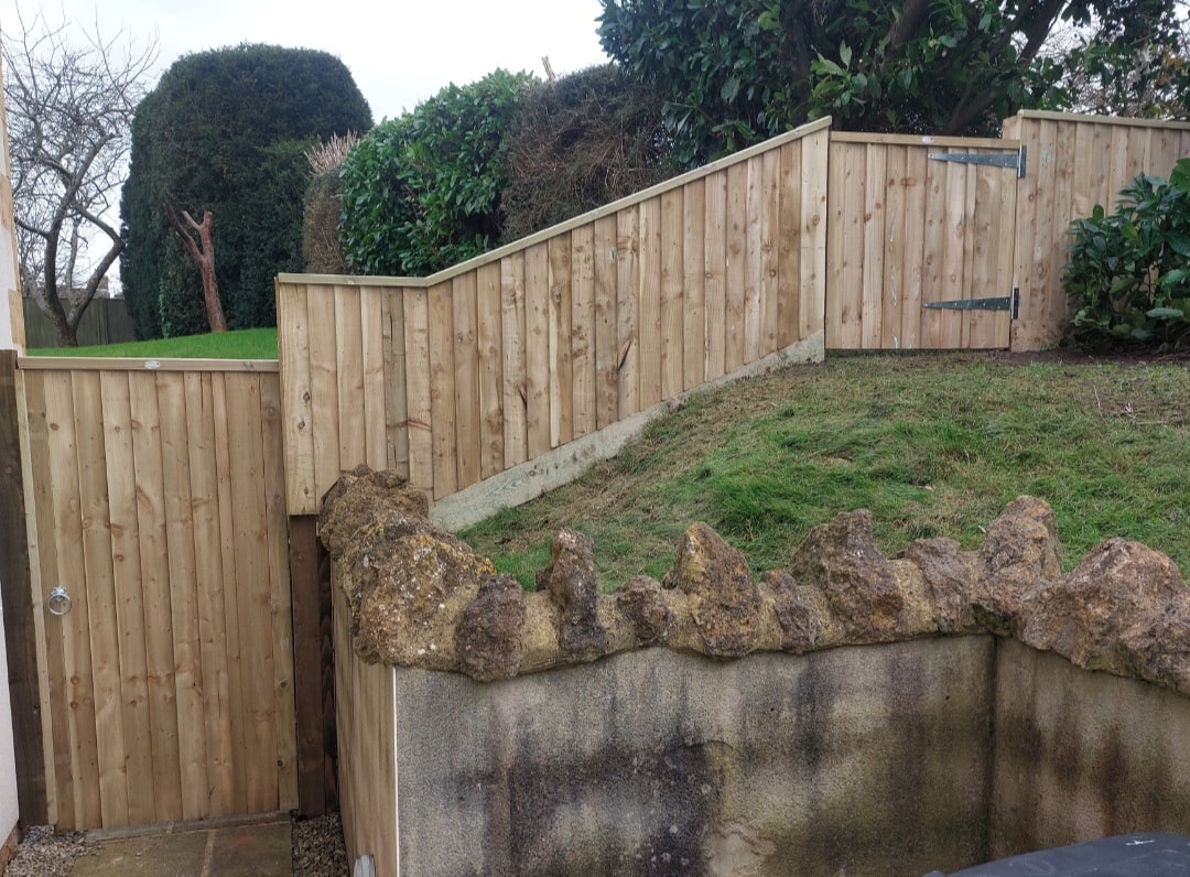 Larch lap fencing with stone retaining wall